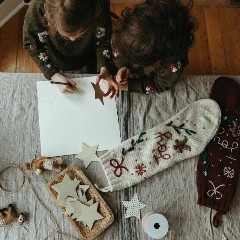 Two children surrounded by various festive decorations, with two different Gingerbread Stockings displayed nearby, showcasing their unique designs and colors in a holiday setting.







