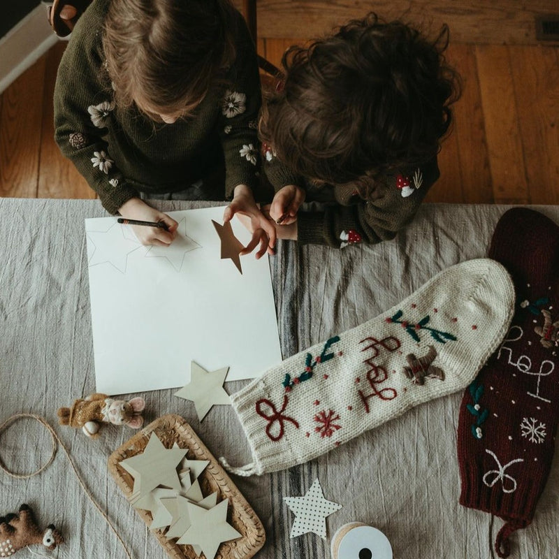 Two children in a festive setting with a few different decorations and products, including the cream white Gingerbread Stocking, showcasing their holiday charm and various designs.