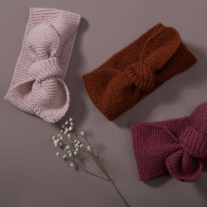 Flat lay picture of hand knitted baby hair band, three piece in three different color : dusty pink, rust and deep berry