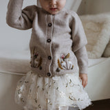 little girl in ballerina skirt and hand knitted and embroidered nude cardigan