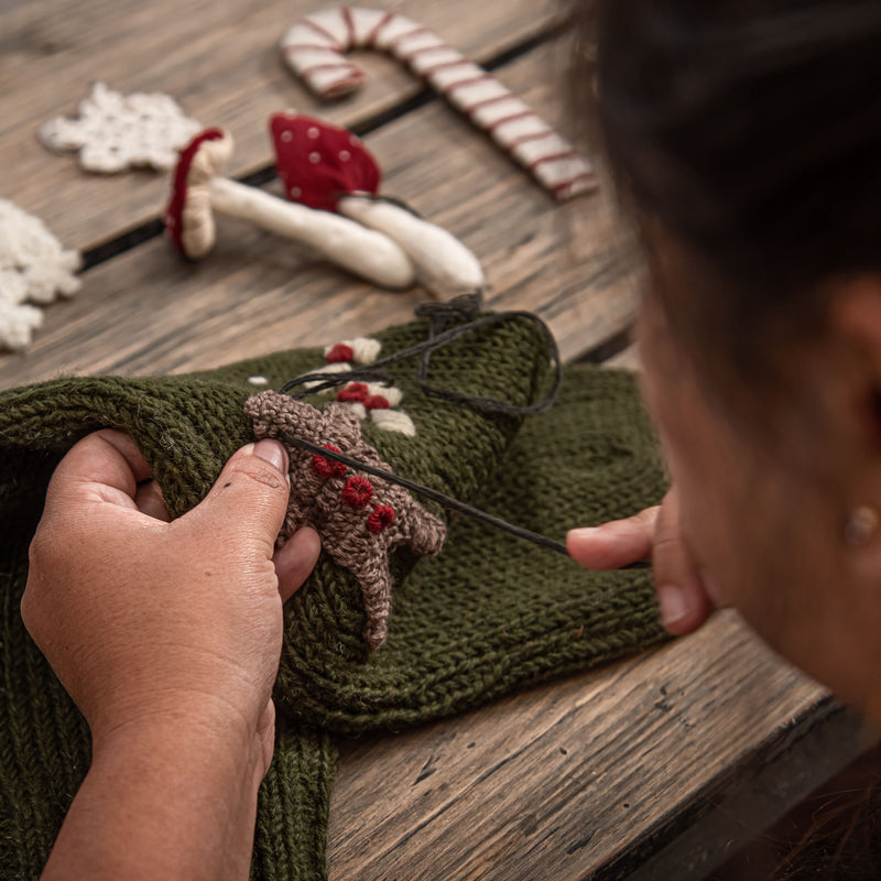 Person knitting a Gingerbread Stocking, focused on their work, showcasing the craftsmanship and detail involved in creating this festive product.







