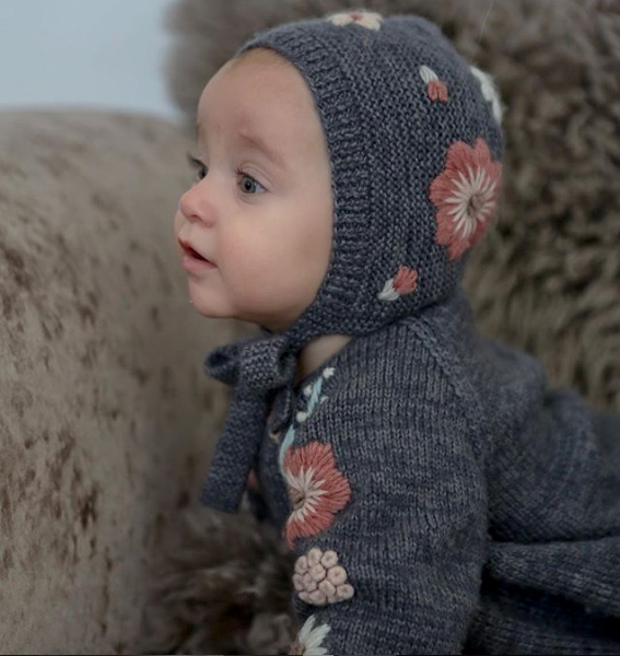 toddler wearing hand knitted floral romper and hand knitted bonnet with beautiful flora embroidery on it