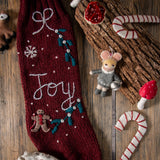 Dark grape Gingerbread Stocking displayed with other festive decorations, showcasing its knitted woolen texture and hand-embroidered JOY/snowflake pattern in a holiday setting.







