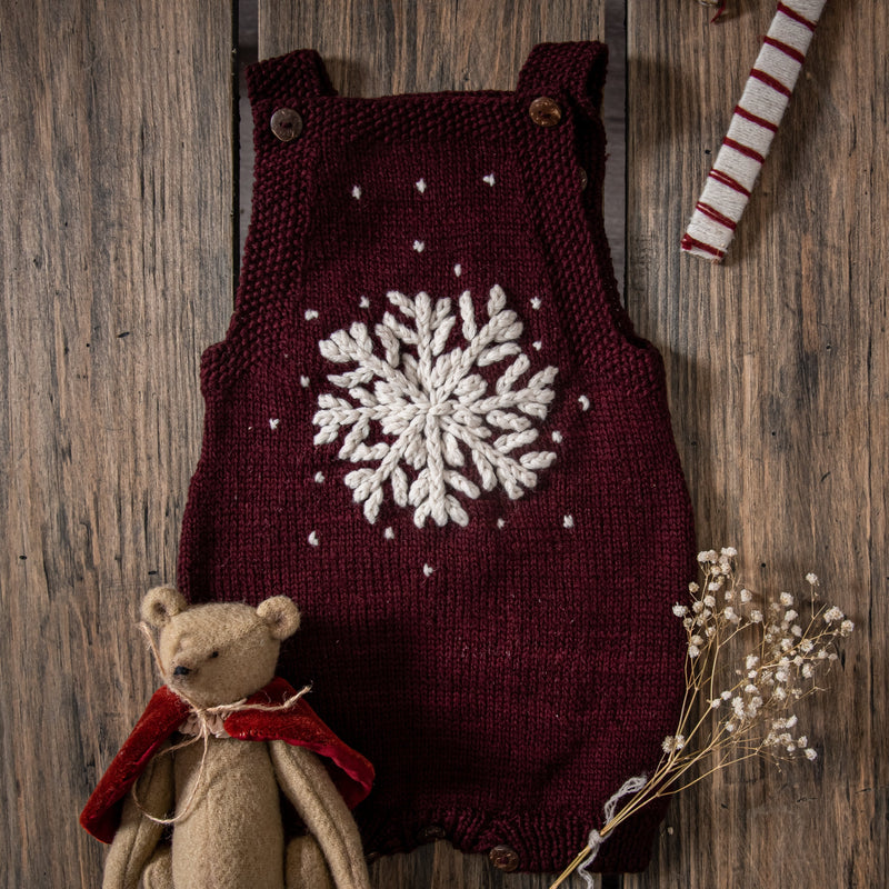 Dark grape hand-knitted snowflake romper displayed on a wooden surface, surrounded by Christmas decorations.