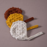 flatlay picture of hand knitted bonet with string ties on bubble styles in rust,mustard and cream white color