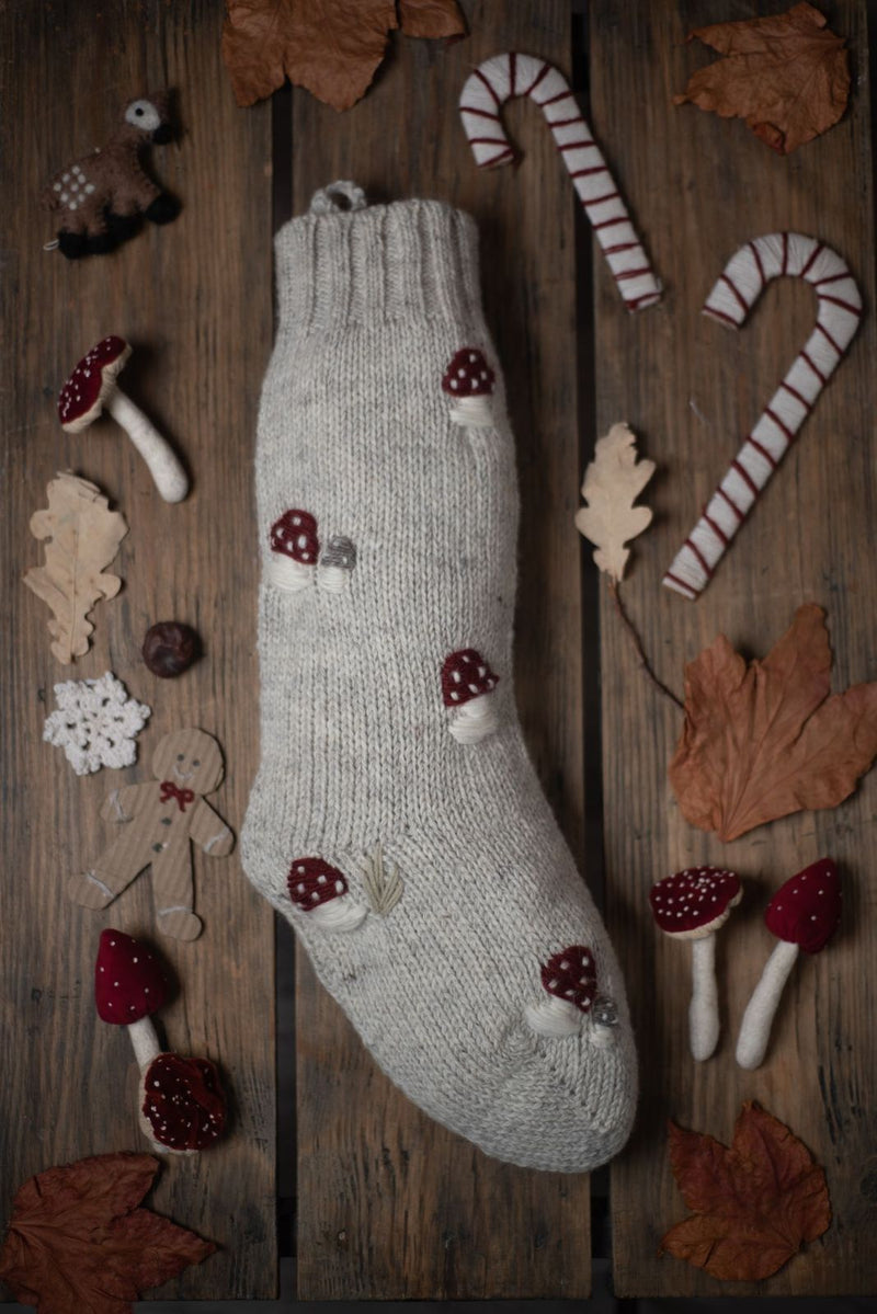 Rye-colored Christmas stocking with hand-embroidered mushroom pattern, placed on a wooden surface in a festive holiday setup.