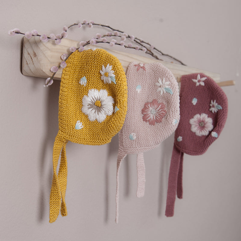Three gorgeous bonnet are hanged in coat rack and they are knitted by hand in our signature vegan cotton, and afterwards we have embroidered this fantastic flower embroidery by hand.
