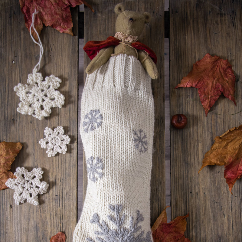 ream White Christmas stocking with hand-embroidered snowflakes, featuring a plush teddy bear peeking out, displayed in a festive holiday setting.