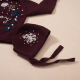 Flat lay image of hand-knitted dark grape bonnet with string ties and matching sweater, showcasing the coordinated design and texture. 