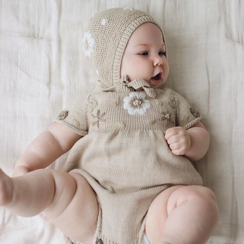 Baby girl wearing hand knitted romper and bonnet with hand knitted floral embroideries on it