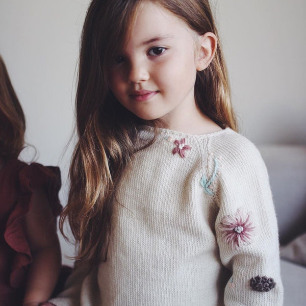 beautiful little  girl wearing hand knitted sweater with floral embroidery on it. She looks really pretty on it.
