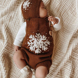 Baby wearing a hand-knitted bonnet with snowflake embroidery and a matching hand-knitted romper featuring a large snowflake design, showcasing the intricate craftsmanship and cozy winter style.