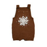 Hand-knitted caramel-colored romper with a large embroidered snowflake on the front and scattered snow details. Features adjustable straps with buttons, perfect for winter play.