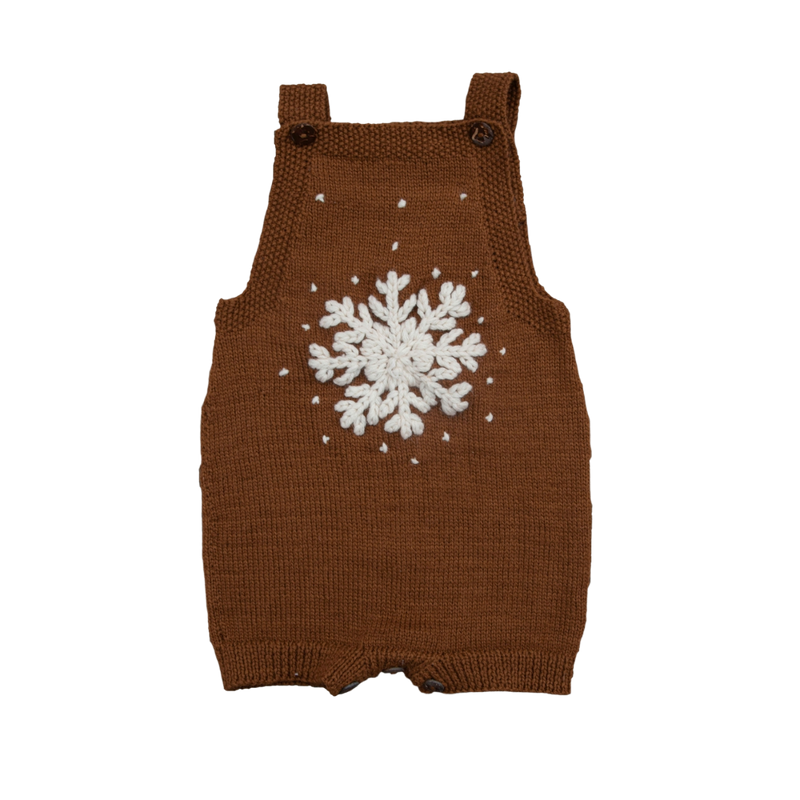 Hand-knitted caramel-colored romper with a large embroidered snowflake on the front and scattered snow details. Features adjustable straps with buttons, perfect for winter play.