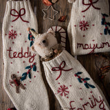 Cream white Gingerbread Stocking alongside several similar stockings and various festive decorations, showcasing their knitted textures and holiday charm in a vibrant setting.







