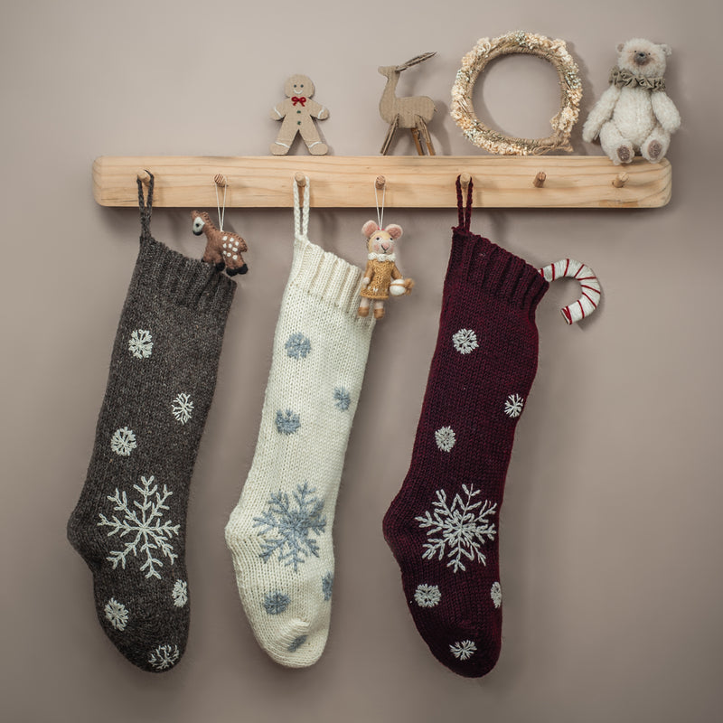 Three hand-knitted Christmas stockings in different colors, including Cream White, hanging in a festive holiday setting, showcasing their unique hand-embroidered patterns.