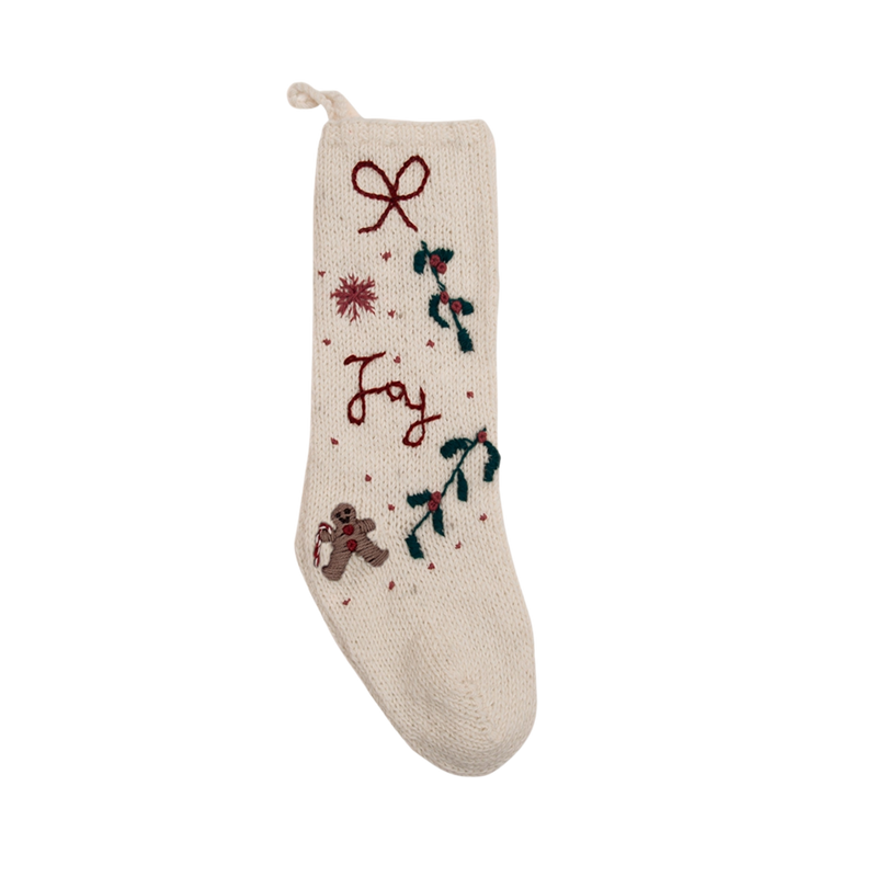 Cream white Gingerbread Stocking with hand-embroidered JOY/snowflake pattern, displayed in a festive setting, showcasing its knitted woolen texture and Christmas charm.