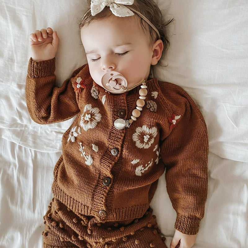 sweet little baby sleeping  wearing our beautifully hand knitted cardigan with floral embroidery on it
